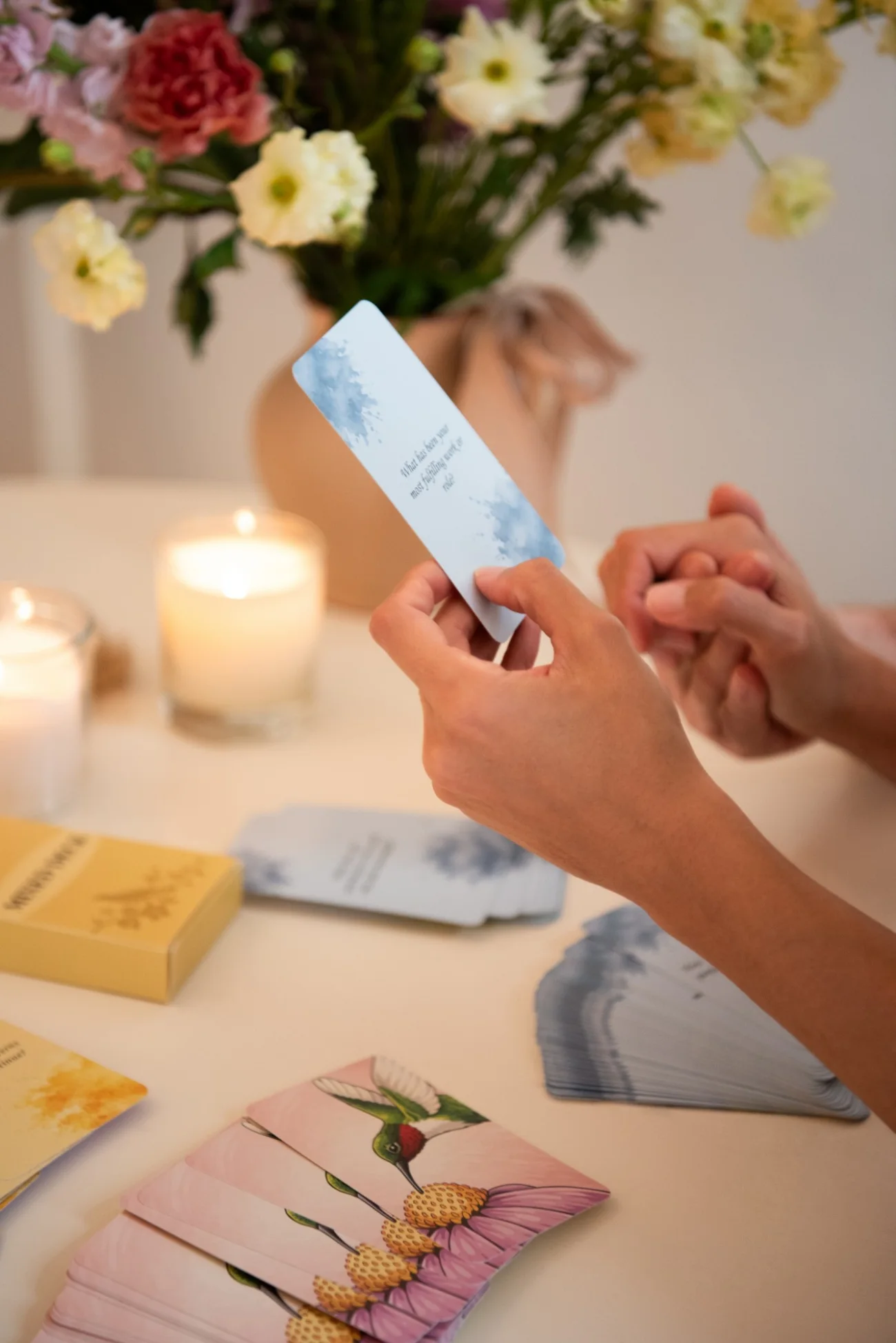 Hands holding a Death Bed Questions card beside candles and flowers