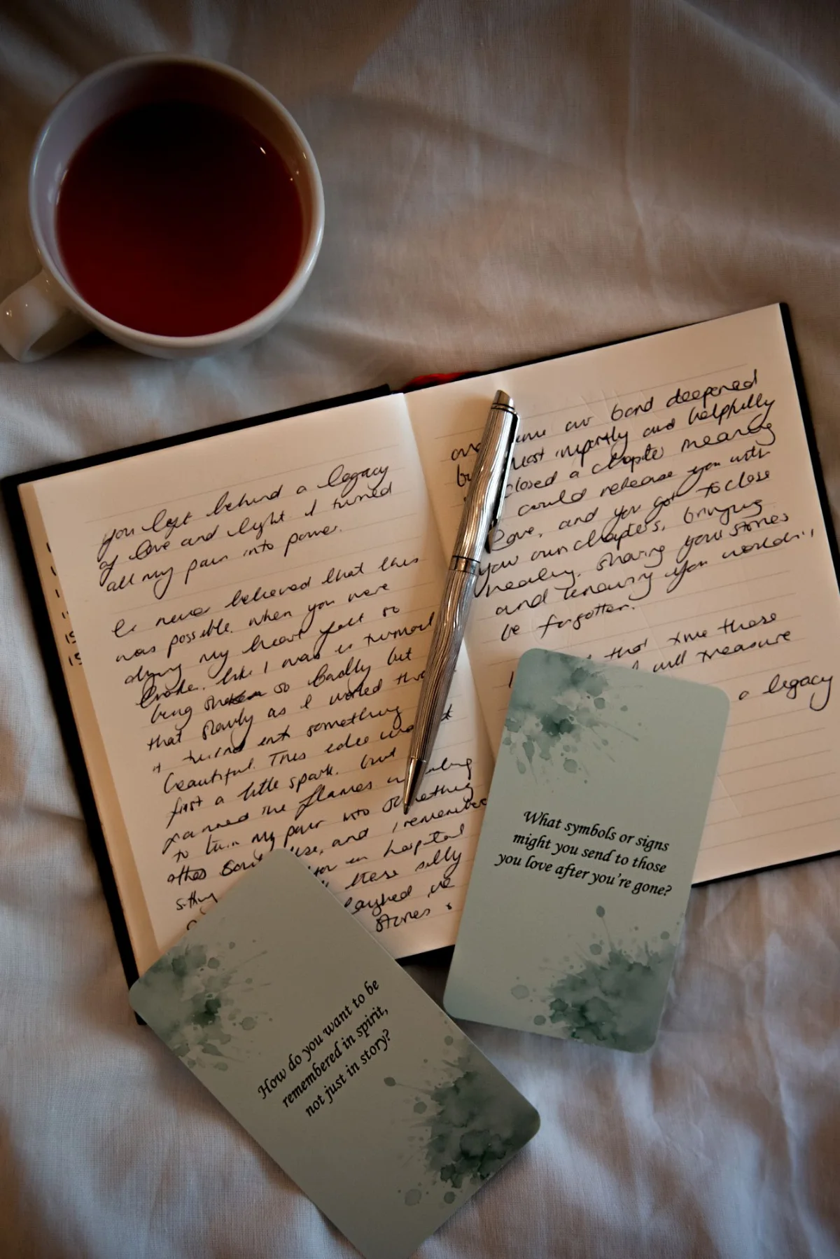Two question cards on an open handwritten journal beside a cup of tea