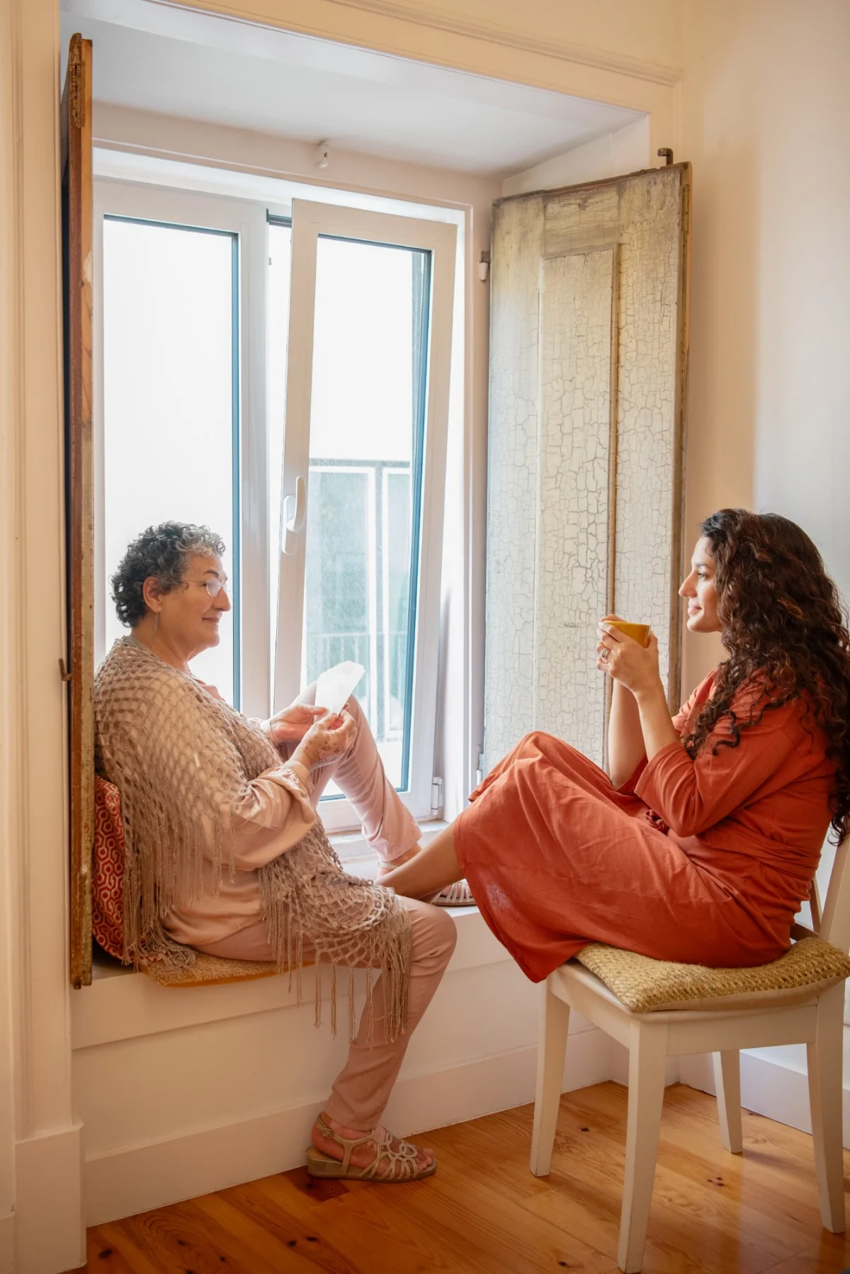 An older woman reading a card to a younger woman by a window
